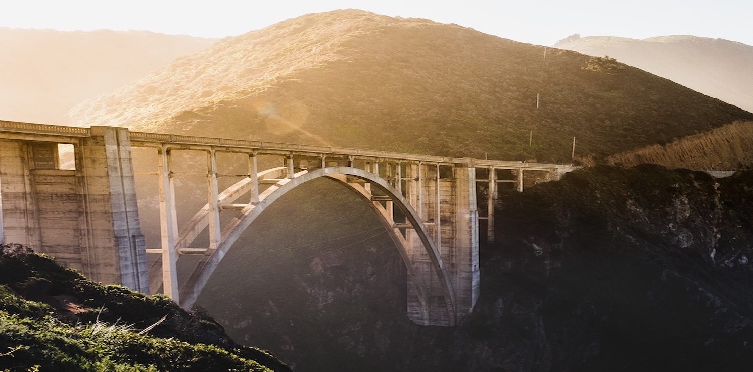 An arched concrete bridge spanning a coastal canyon at sunset